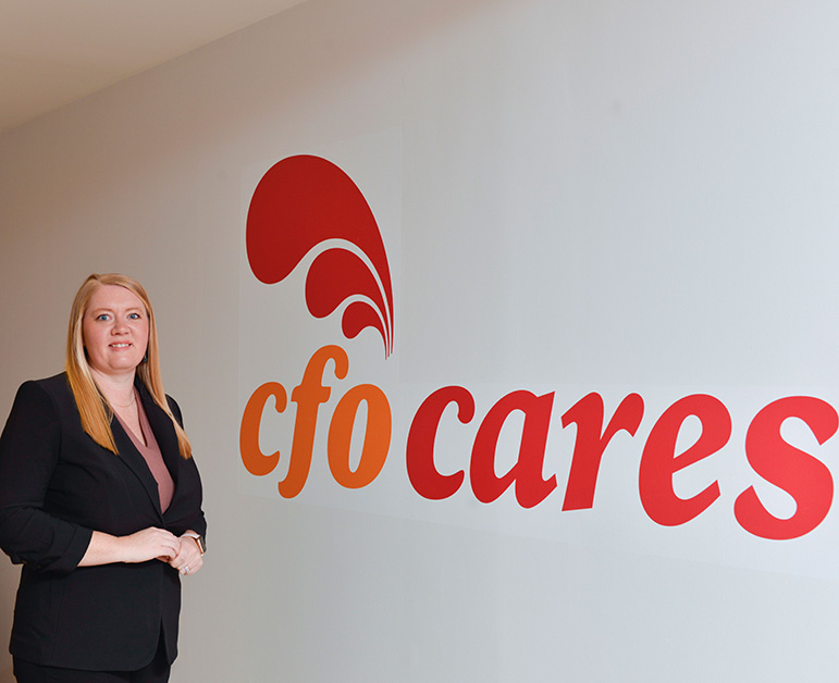 Andrea Veldhuize standing next to a CFO cares wall-mounted logo